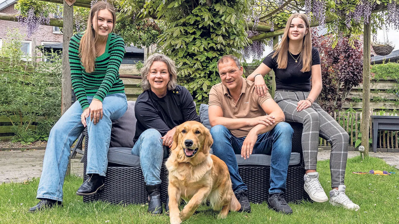 Familie van de meer poseren samen met KNGF hond Houbi zittend op een bank in de tuin
