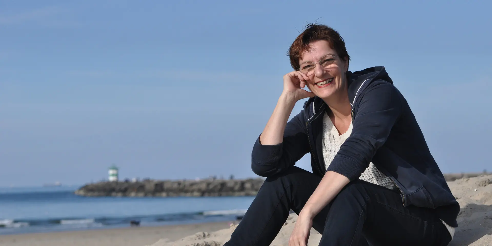 Petra kijkt naar de camera met op de achtergrond het strand en de zee