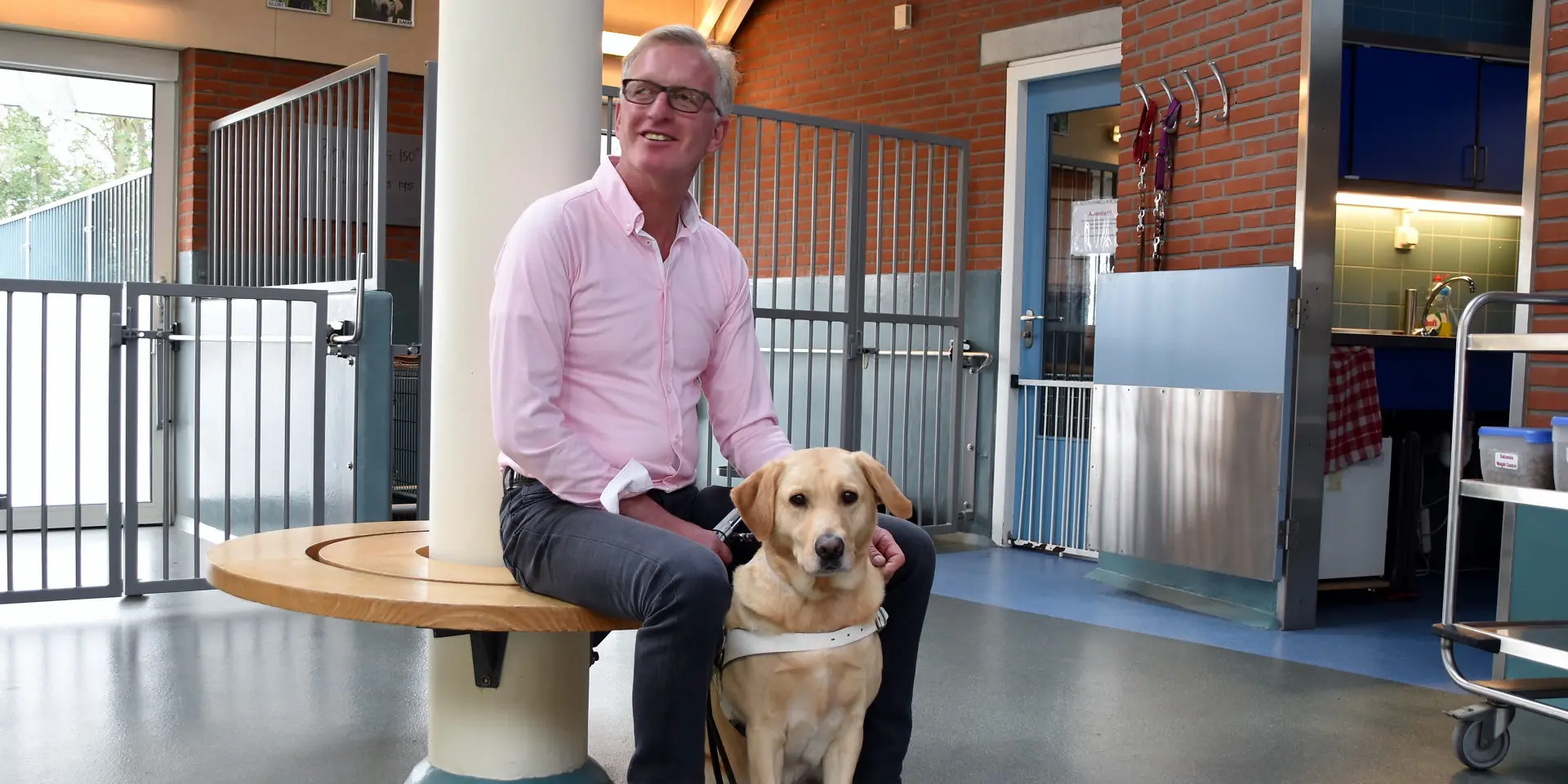 Willem zit op een bank met zijn hulphond in de kennel van KNGF