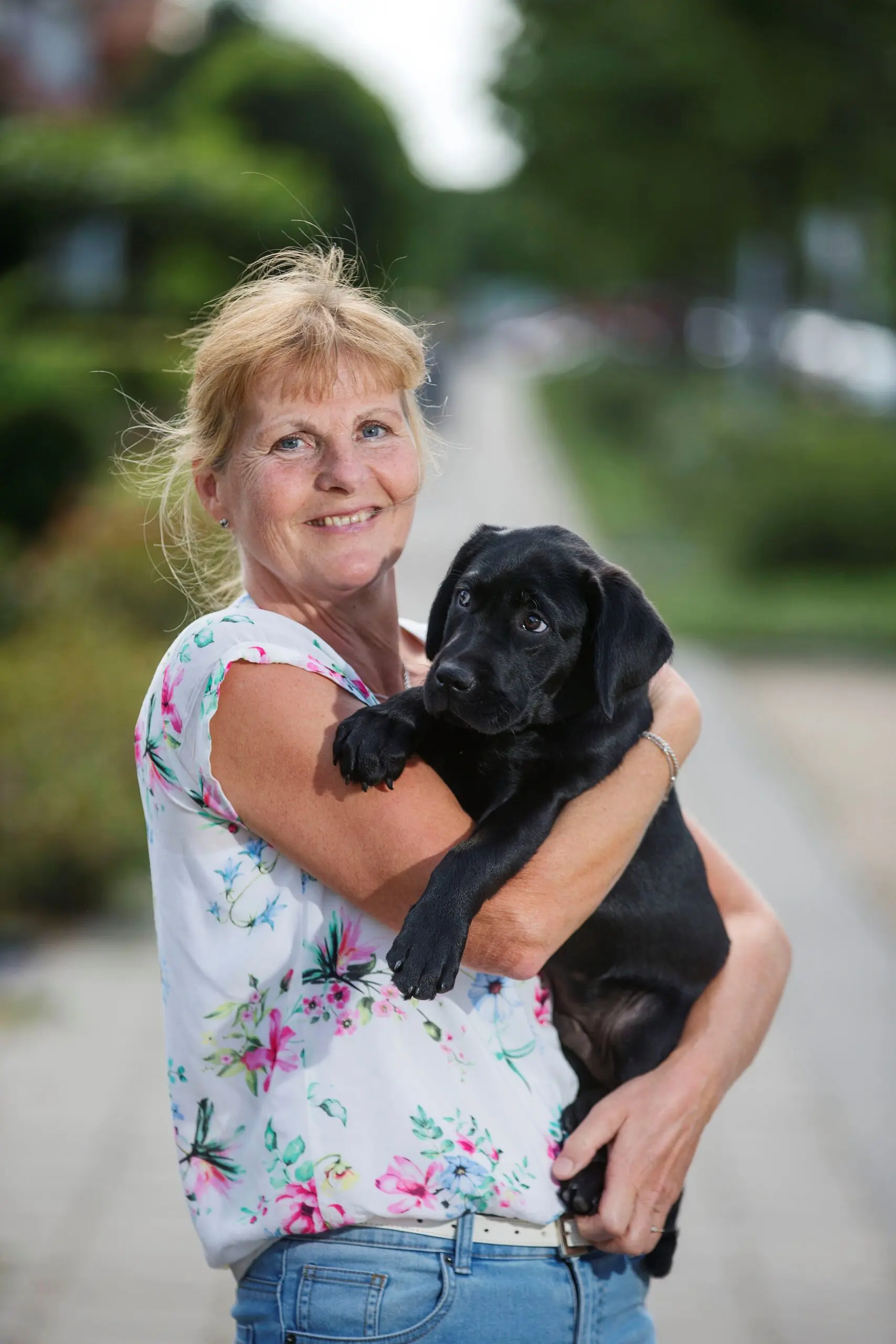 Pleegouder Margreet houdt zwarte labrador pup Jovi vast en poseert voor de fotograaf