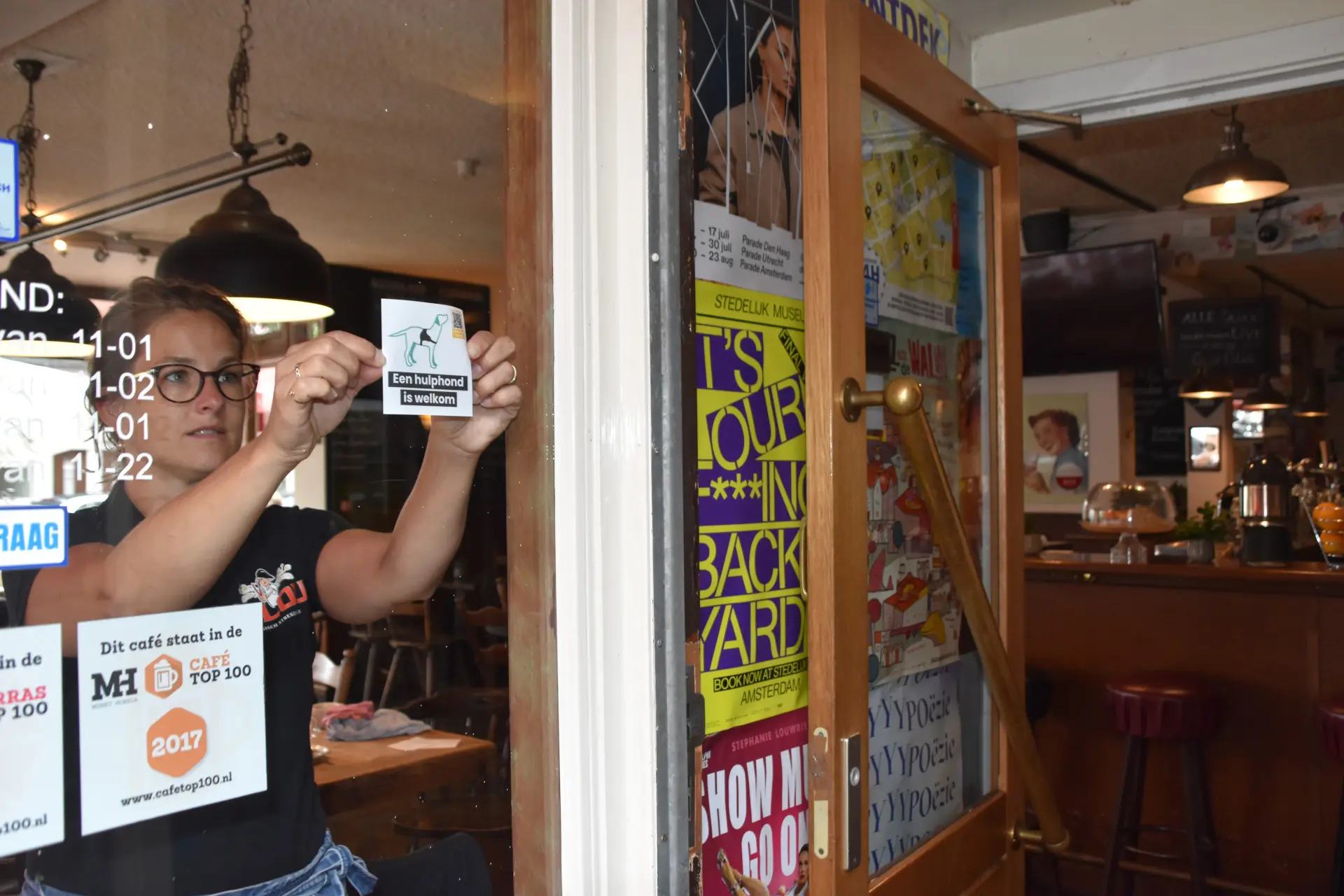 vrouw plakt hulphond-is-welkom sticker op het raam