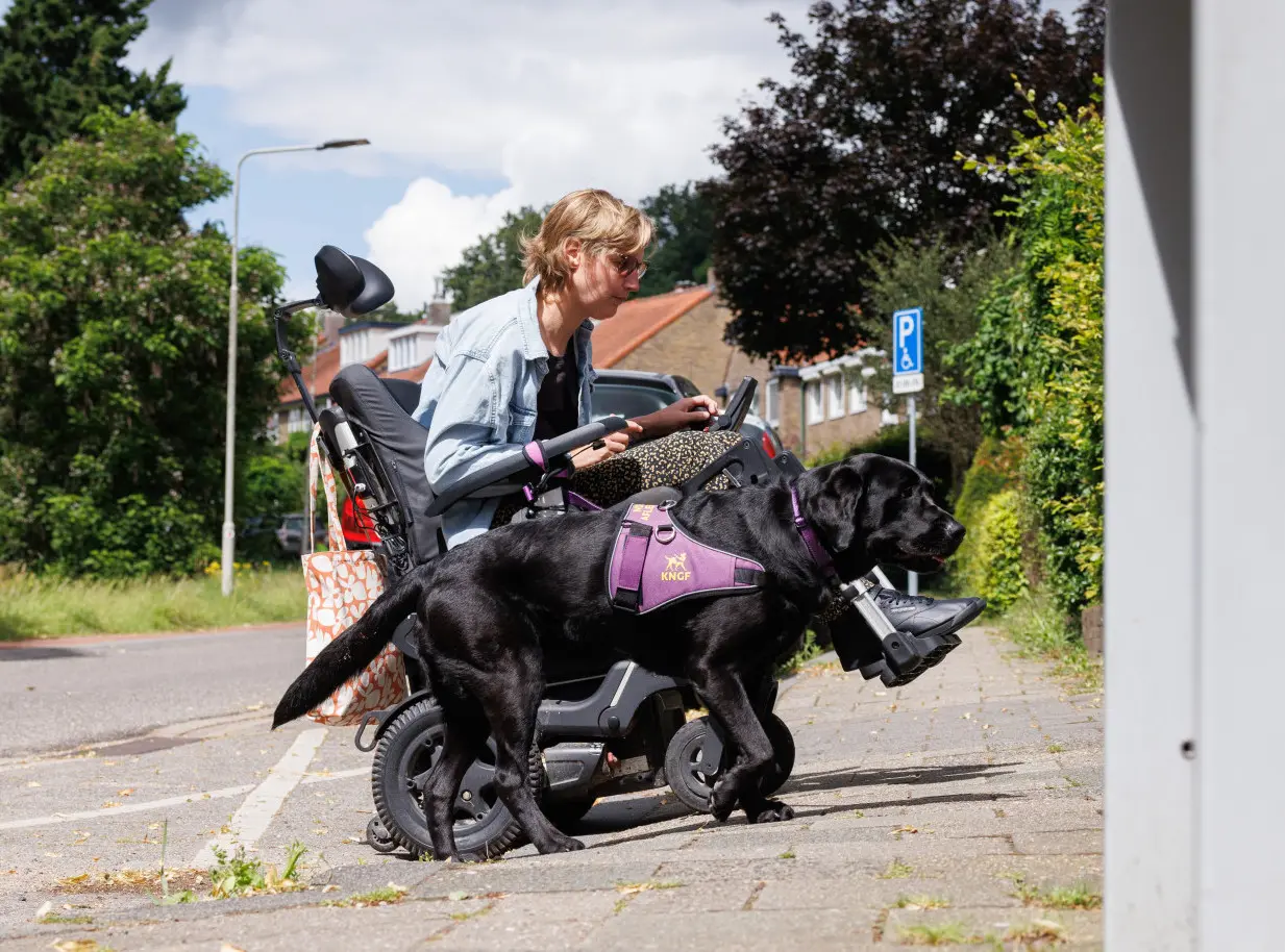 Nynke rijdt een stoep op in haar rolstoel met haar assistentiehond Jissa naast haar