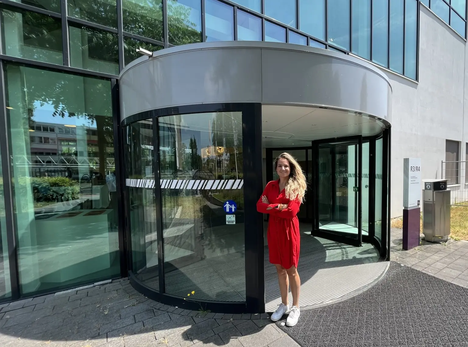 Jennifer staat naast een draaideur van de hogeschool waar een sticker is geplakt dat hulphonden welkom zijn