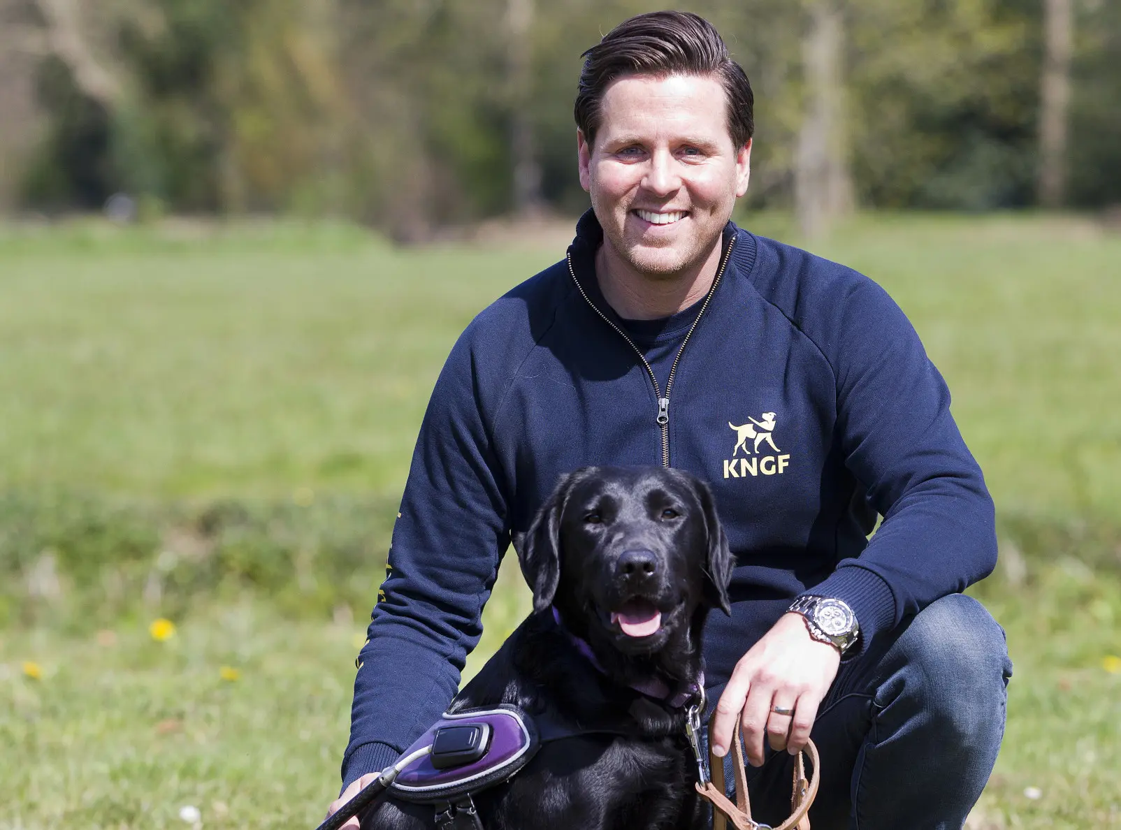 Trainer Menno en blindengeleidehond Usmay poseren op een veld