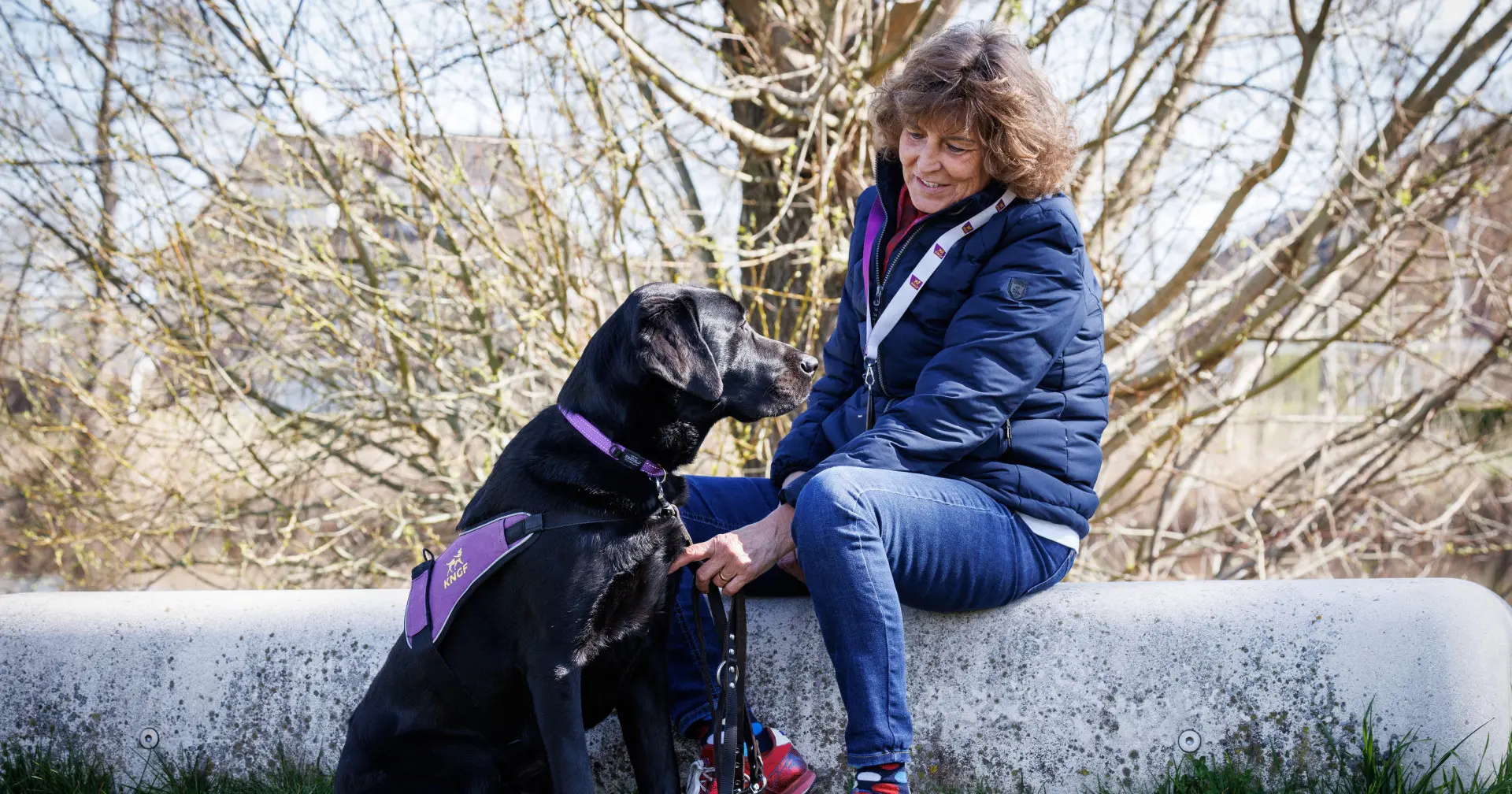 Mellina zit op een betonnen rand terwijl assistentiehond Lyos voor haar zit