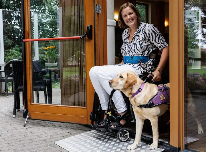 Mayke en haar assistentiehond Roos in de deuropening van een restaurant waar een hulphond welkom is