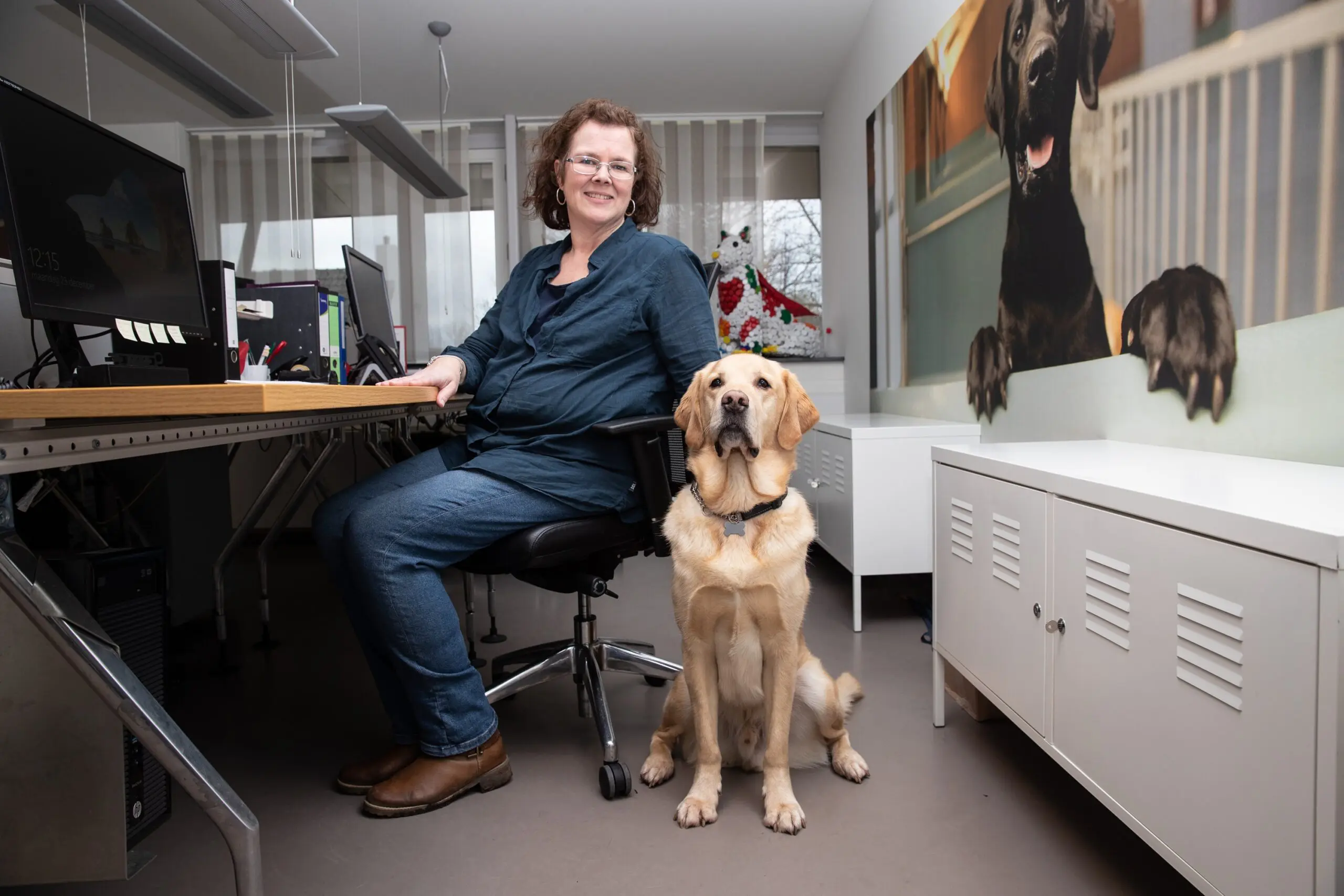 vrouw zit achter bureau met naast haar een blonde hond