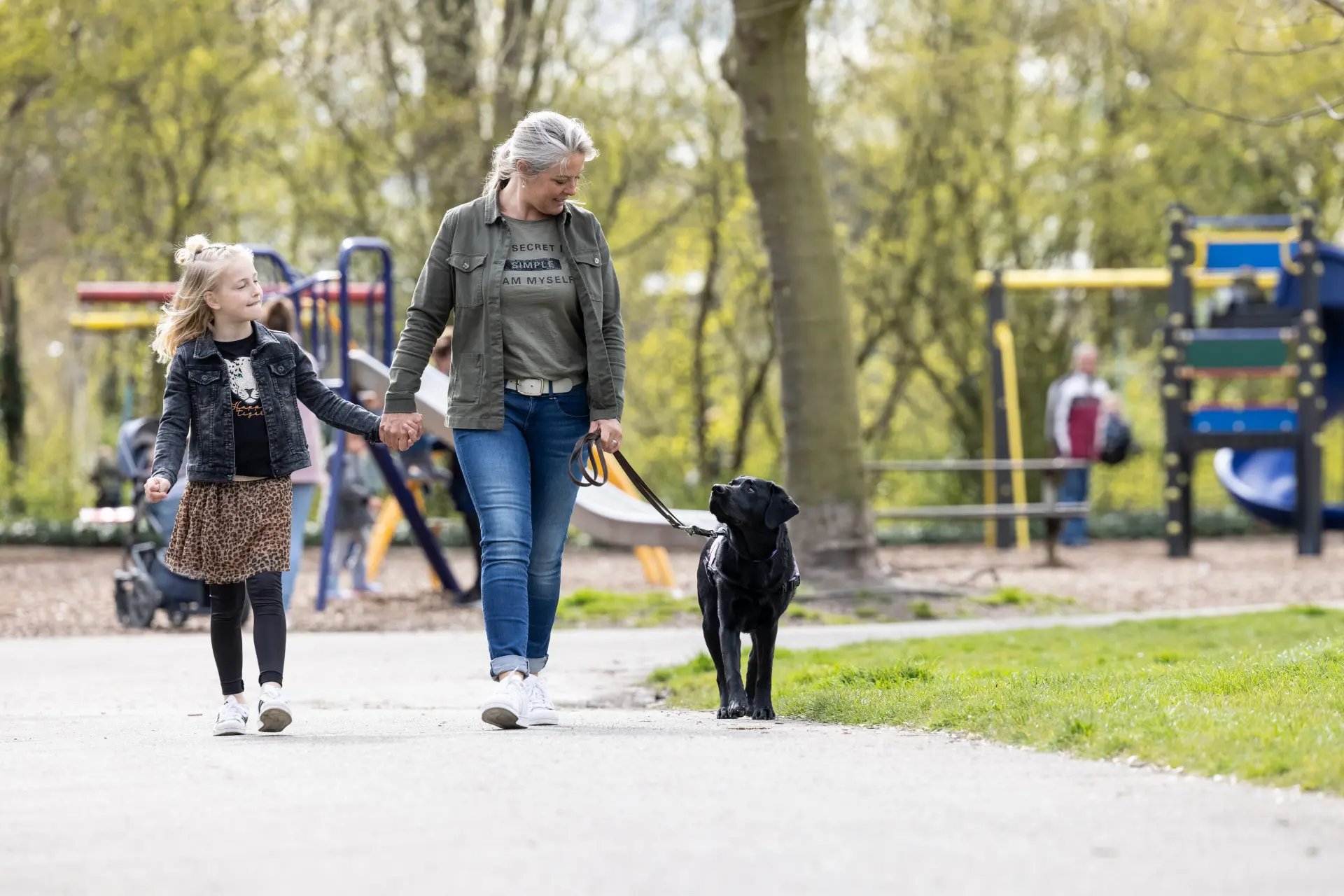 Angela loopt in het park met haar dochter aan de hand, in de andere hand heeft ze haar PTSS assistentiehond Rotar vast