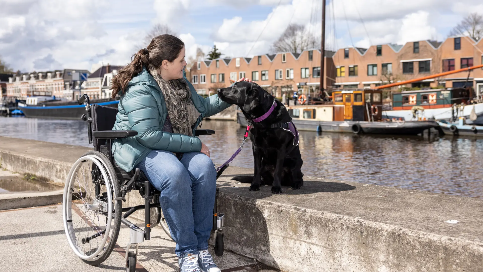 Assistentiehond Entli samen met Bente aan de oeverkant van het water, waar Bente op een betonnen rand zit
