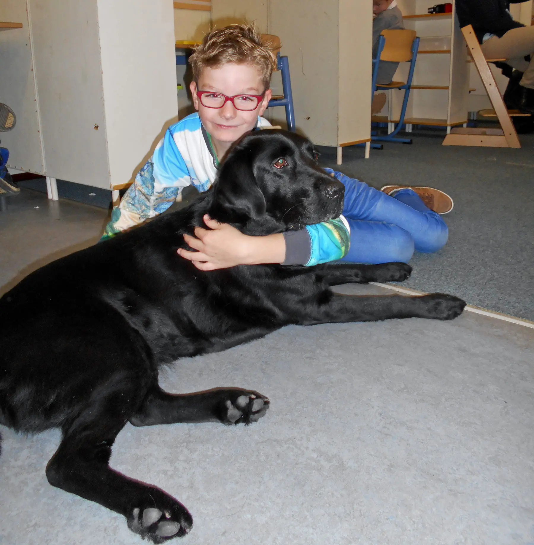 Corwin zit op de grond met zijn hulphond Judi, een zwarte labrador