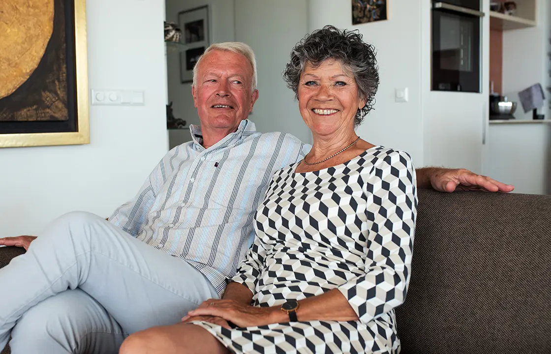 Evert en Lidwien zitten samen op de bank en kijken naar de camera