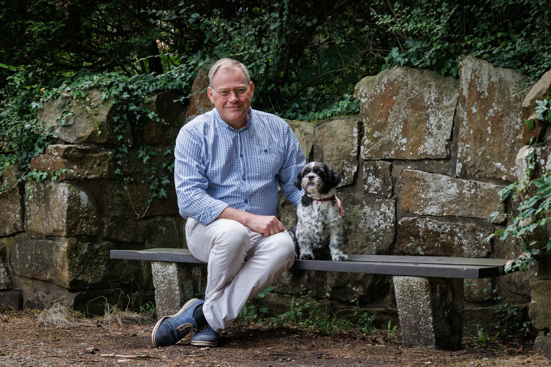 Martin zit op een stenen bankje, met een stenen muur achter zich en naast hem zit zijn eigen hond