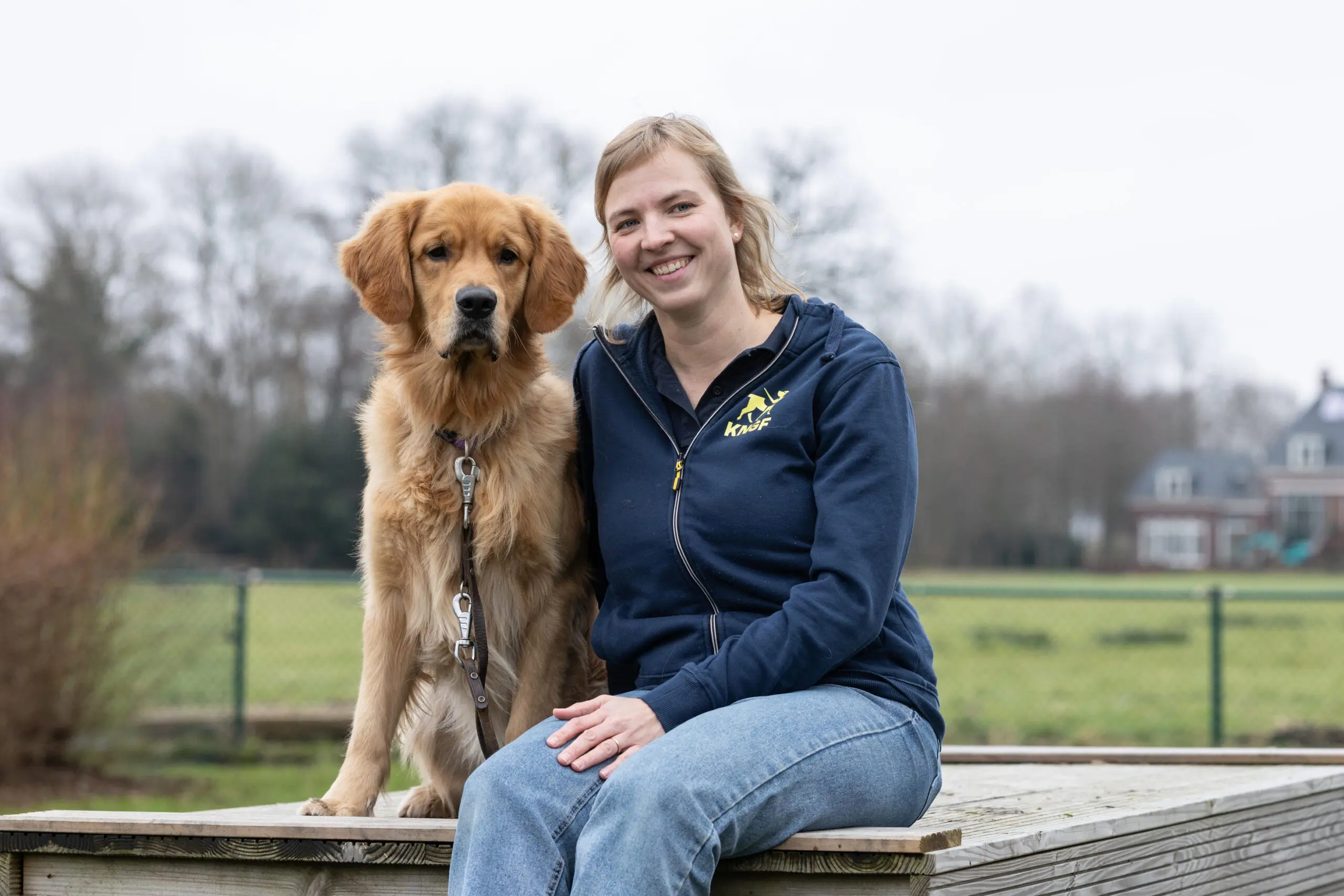 Esther, werkzaam als fokspecialist bij KNGF Geleidehonden, samen met golden retriever Hugo op een bankje.