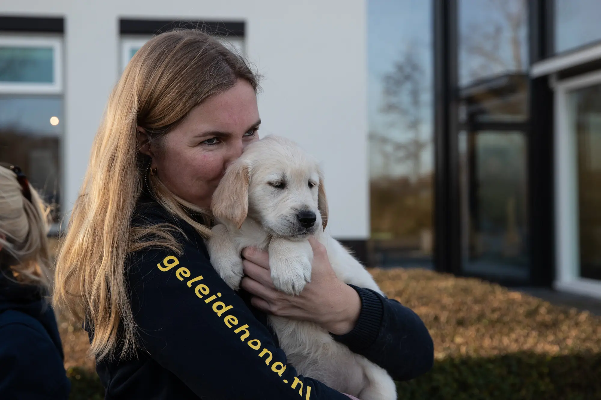 vrouw in KNGF-kleding knuffelt een golden retriever pup