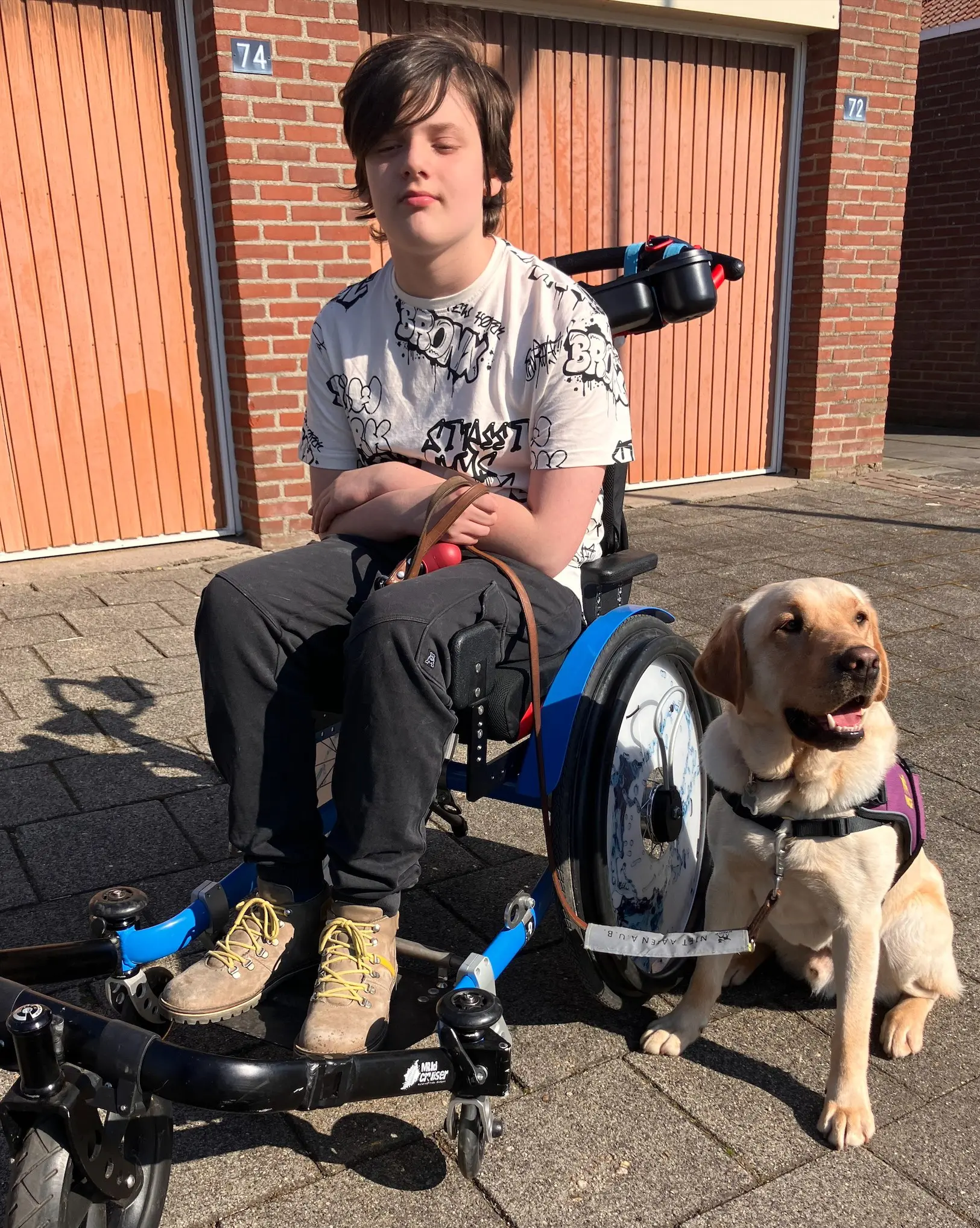 portret buiten van een jongen in een rolstoel en naast hem een blonde labrador in een kngf-dekje.