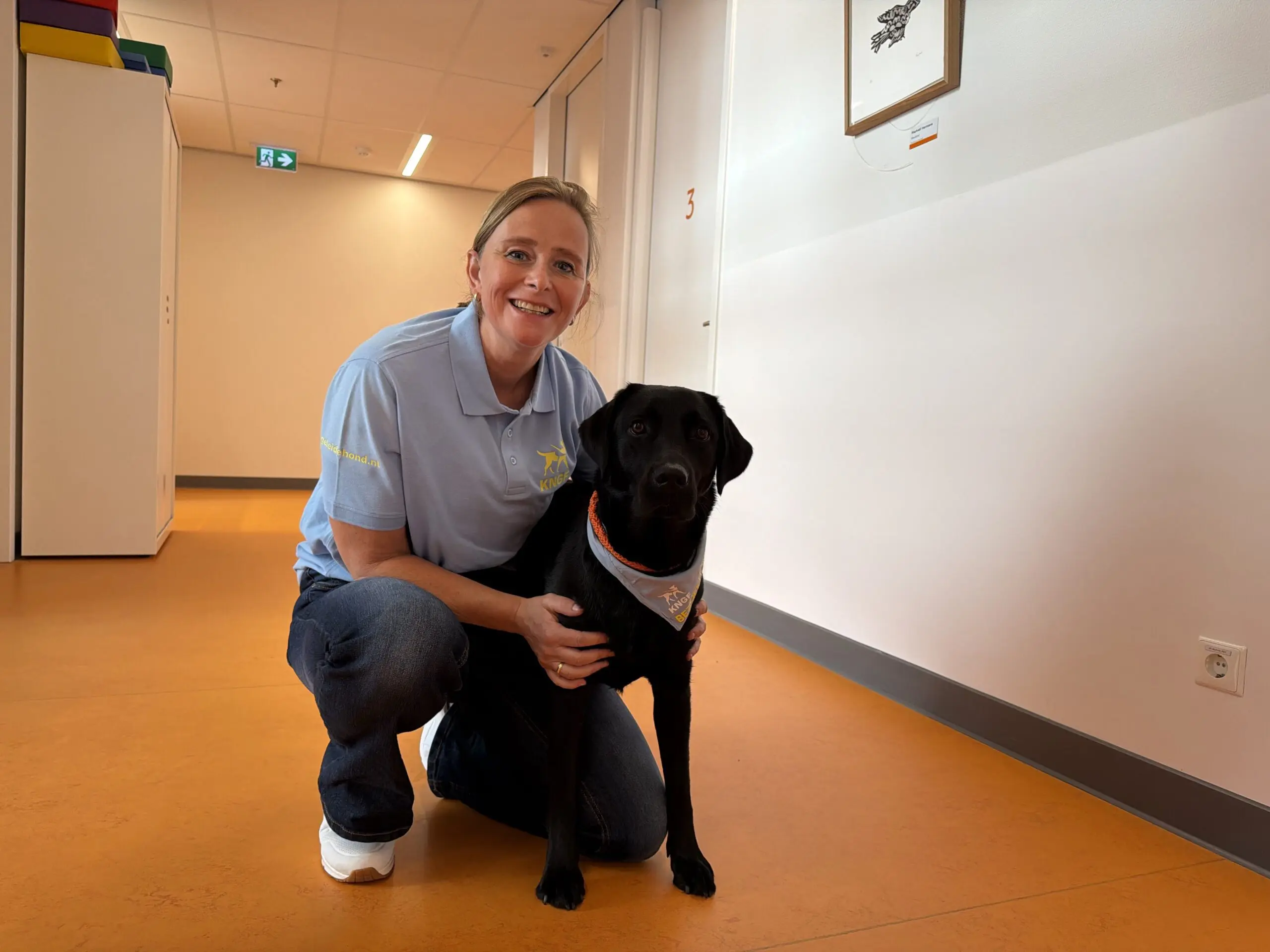 Bezoekhondenteam Barbara met haar zwarte labrador Fenna zitten gehurkt naast elkaar