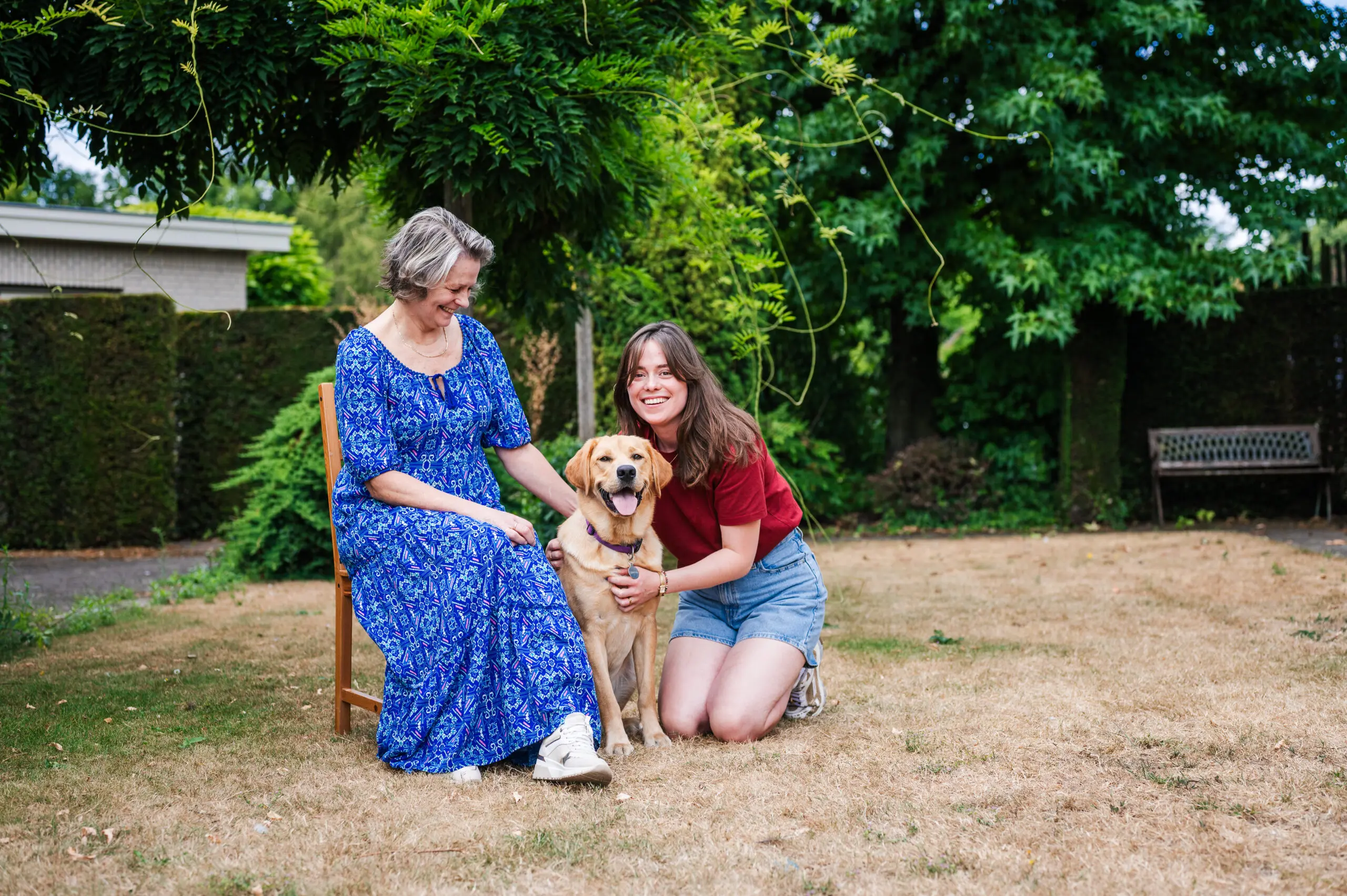 vrouw en dochter zitten samen buiten, ze knuffelen een blonde hond