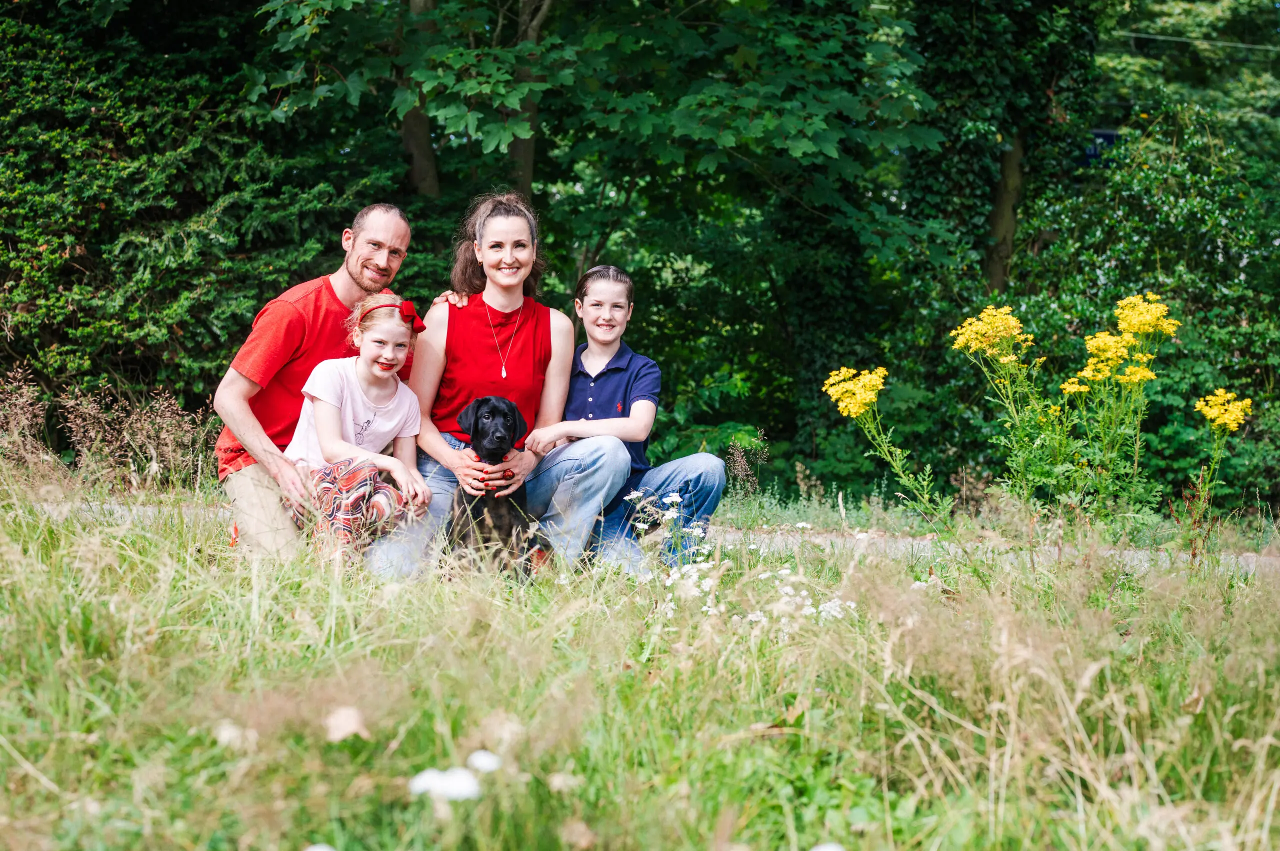 gezin met man, vrouw en 2 kinderen zitten buiten in een grasveld met een kleine zwarte pup
