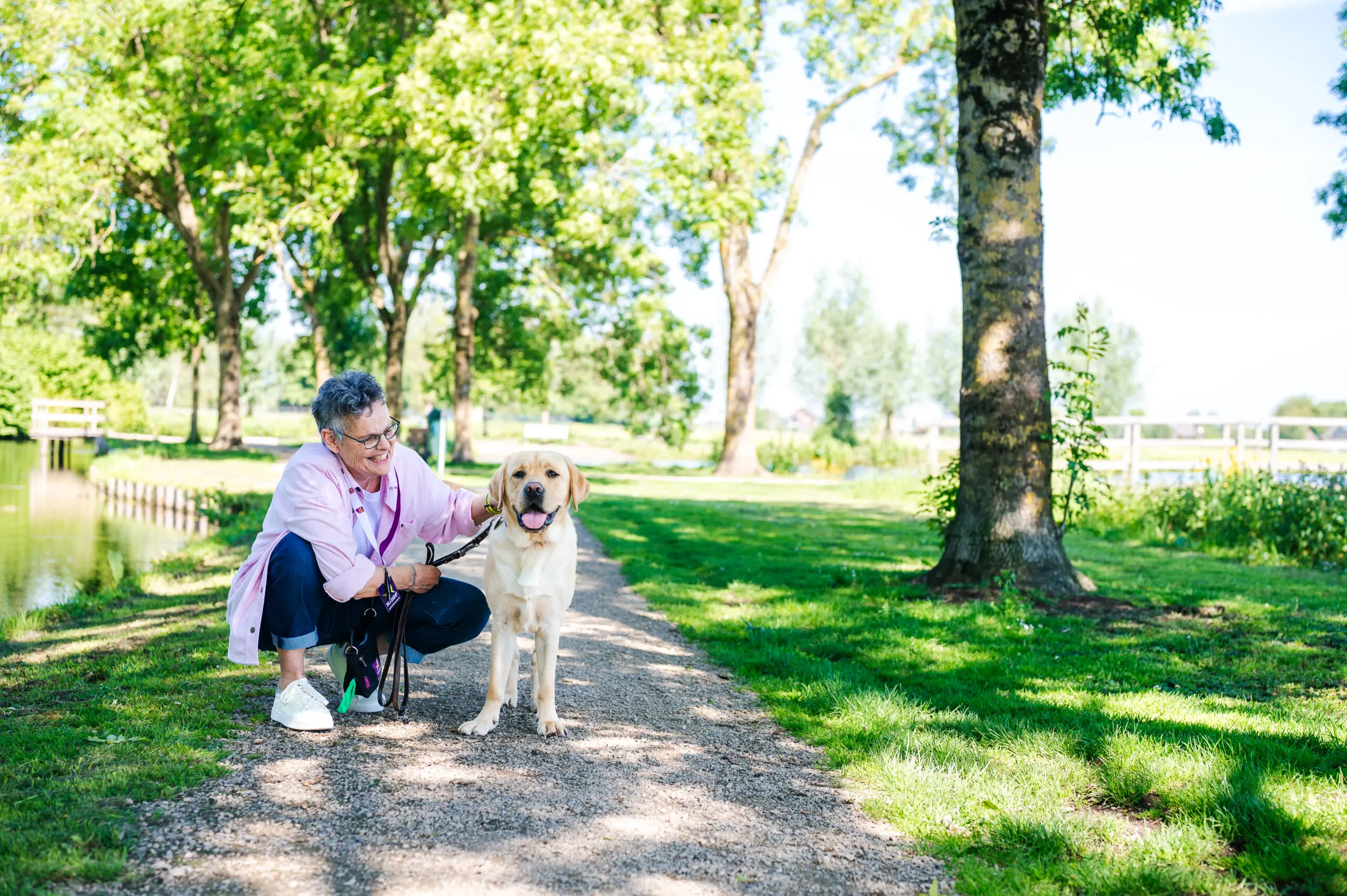 vrouw buiten in een park aait een staande blonde jonge hond