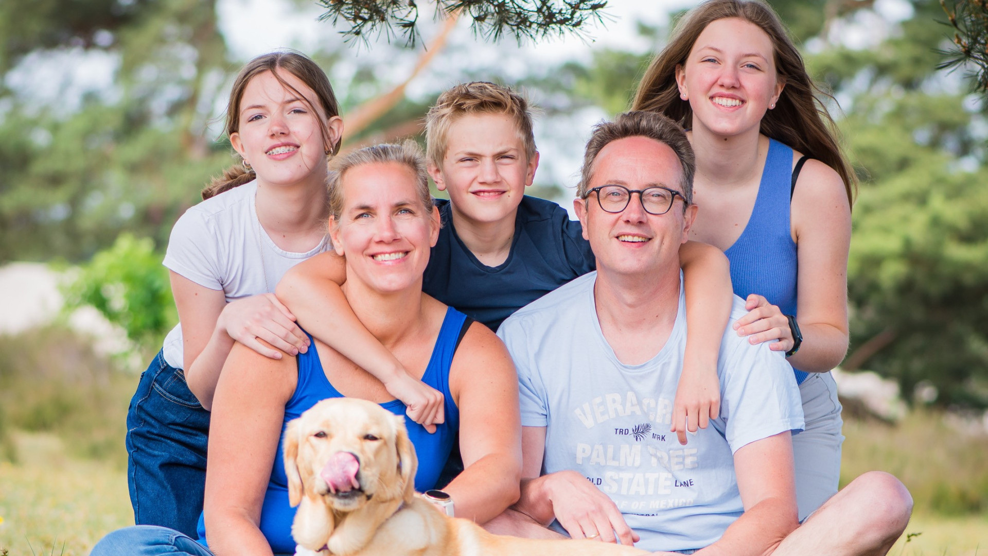 Familie verkerk poseert samen met een jonge KNGF hond met op de achtergrond een natuur omgeving.