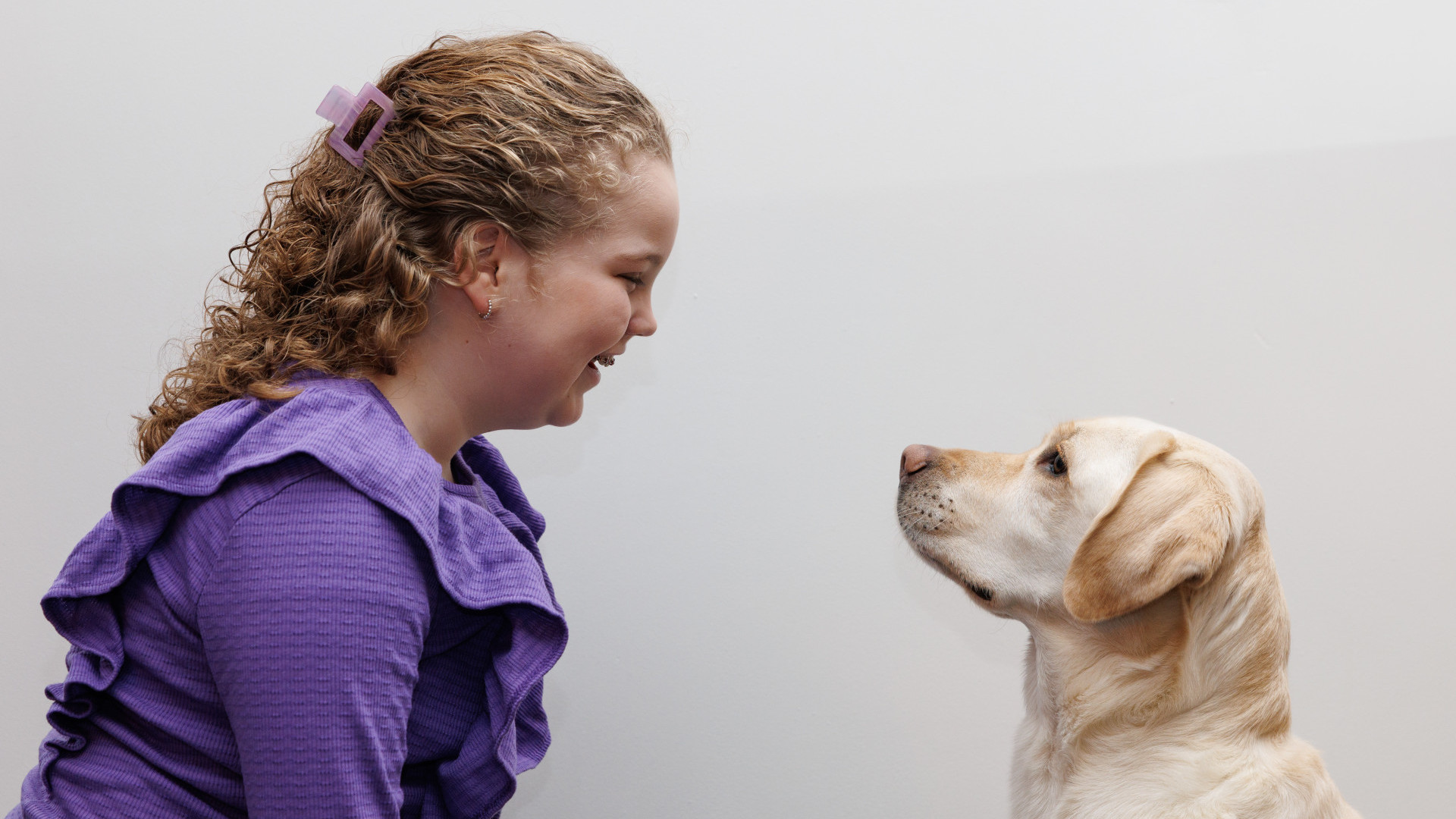 Meisje en blonde hond zitten tegenover elkaar en kijken elkaar lief aan