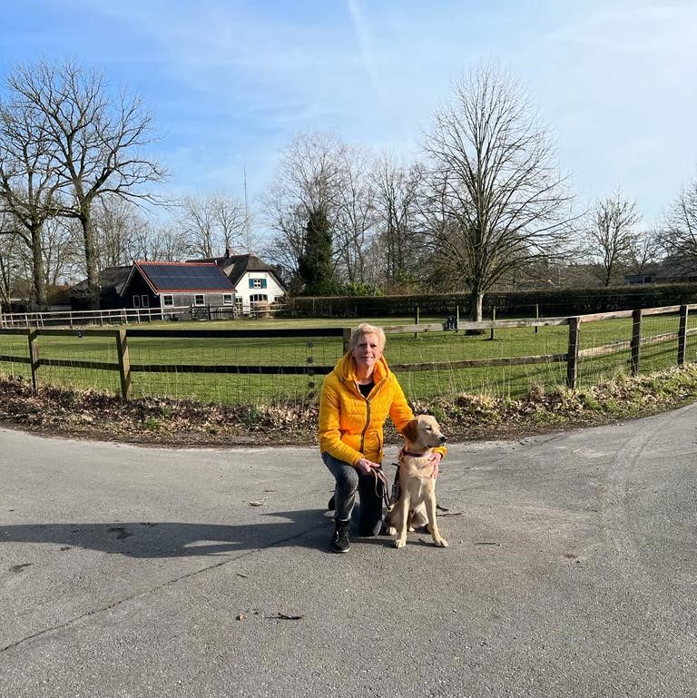 Christien samen met KNGF pup Arkos op de oprijlaan met in de verte een boerderij.